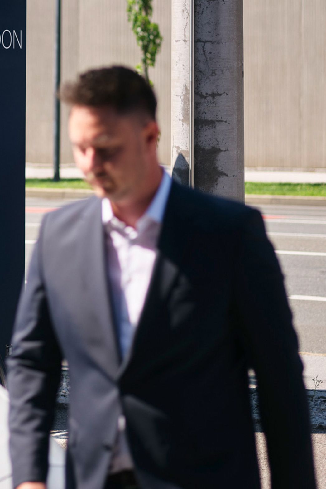 Moški hodi mimo električnega vozila pred hitro polnilno postajo.