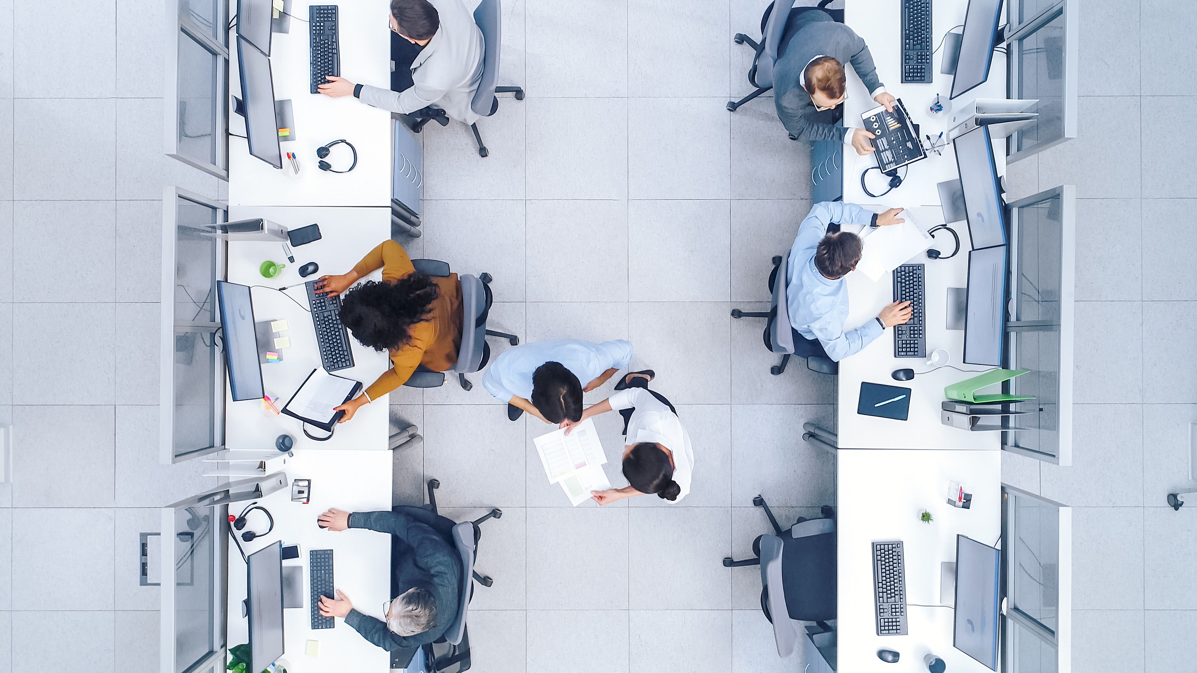 Pogled iz ptičje perspektive na pisarno, kjer več ljudi dela za svojimi računalniki.