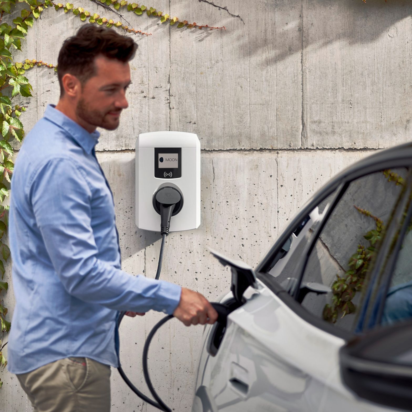 Moški pred stavbo priklaplja električni avto na stensko polnilnico.