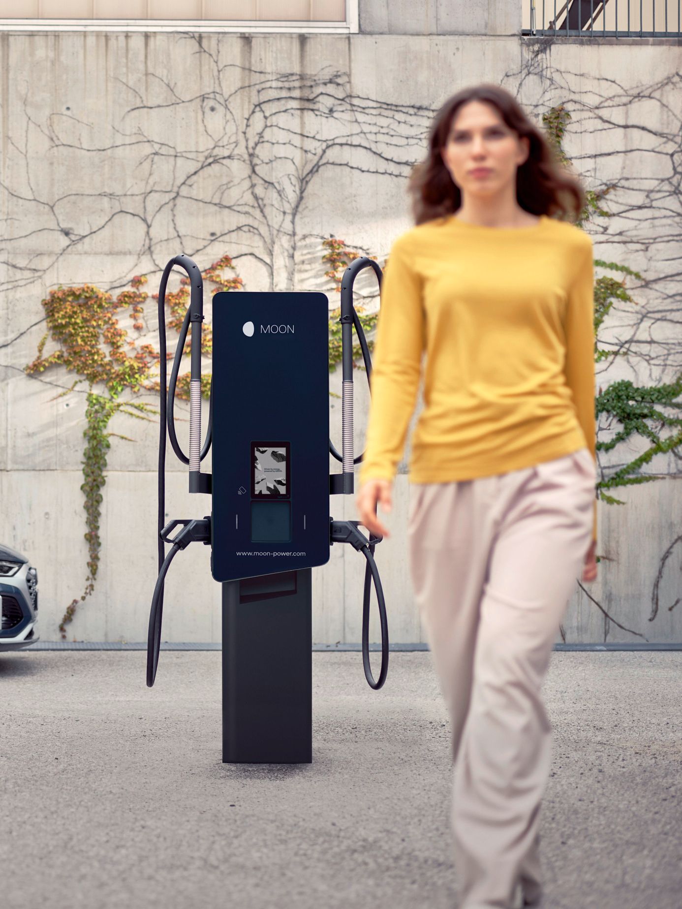 Woman walks in front of a wallbox with an electric car in the background