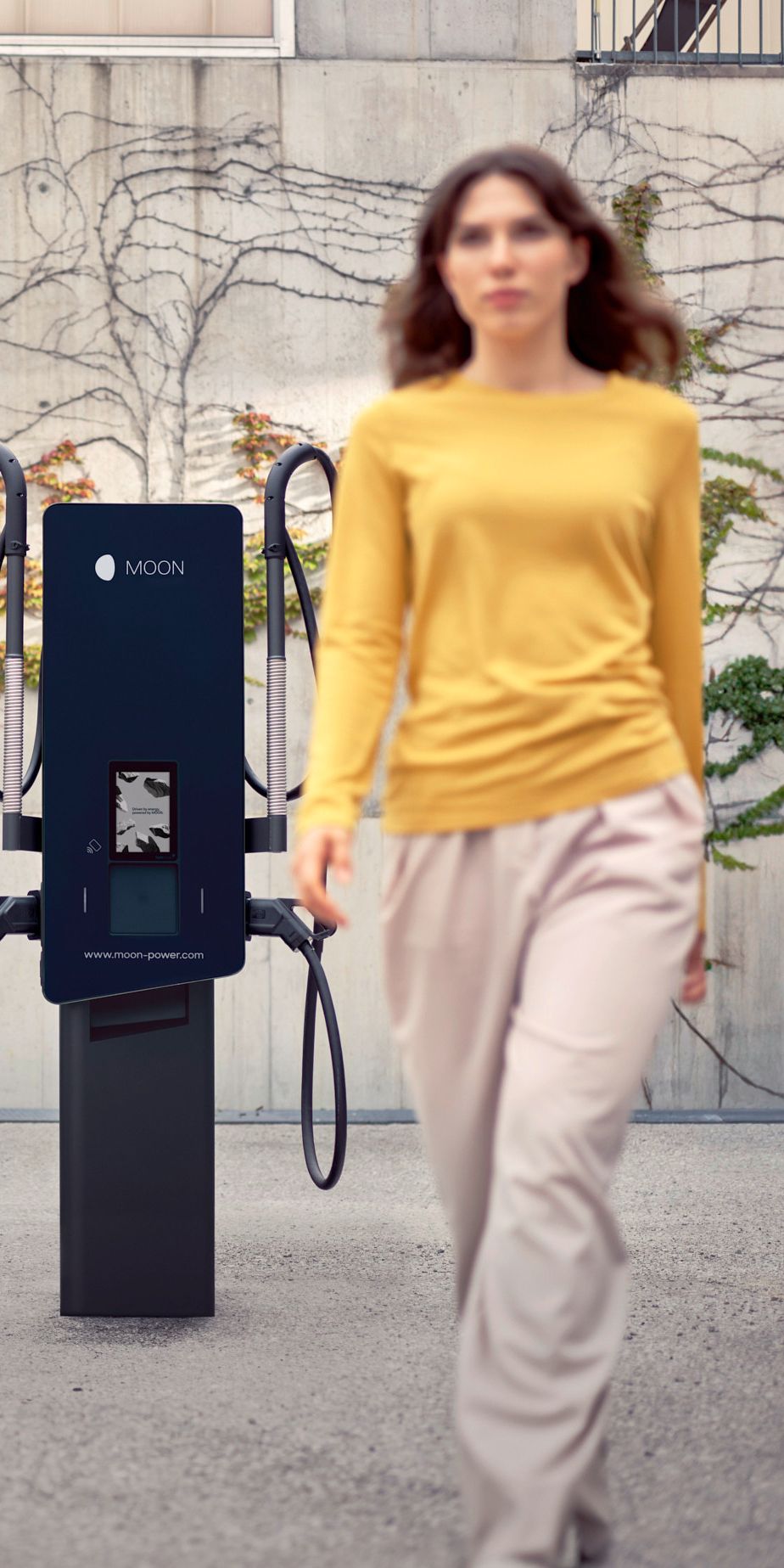 Woman walks in front of a wallbox with an electric car in the background