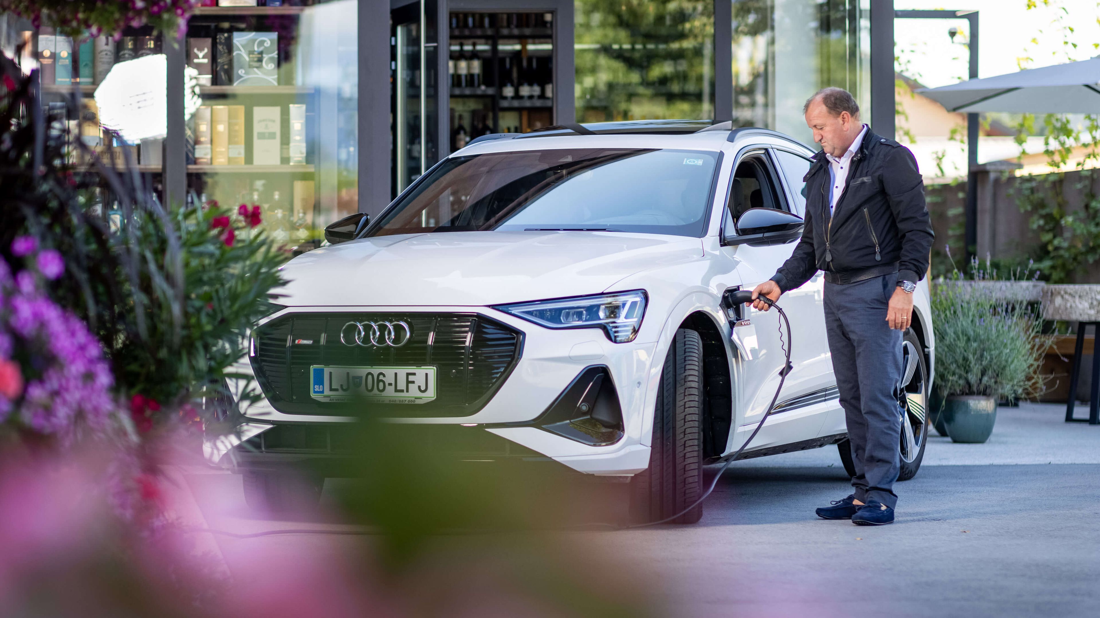 Moški pred stavbo priklaplja električni avto na polnilno postajo.