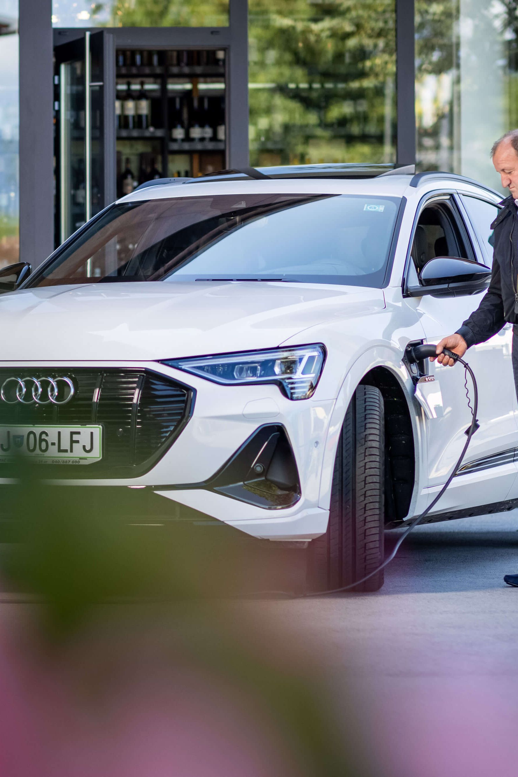 Moški pred stavbo priklaplja električni avto na polnilno postajo.