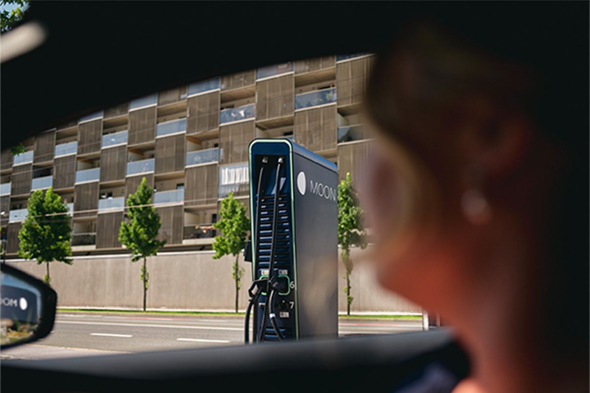 Oseba sedi v avtu, v ozadju pa hitro polnilna postaja