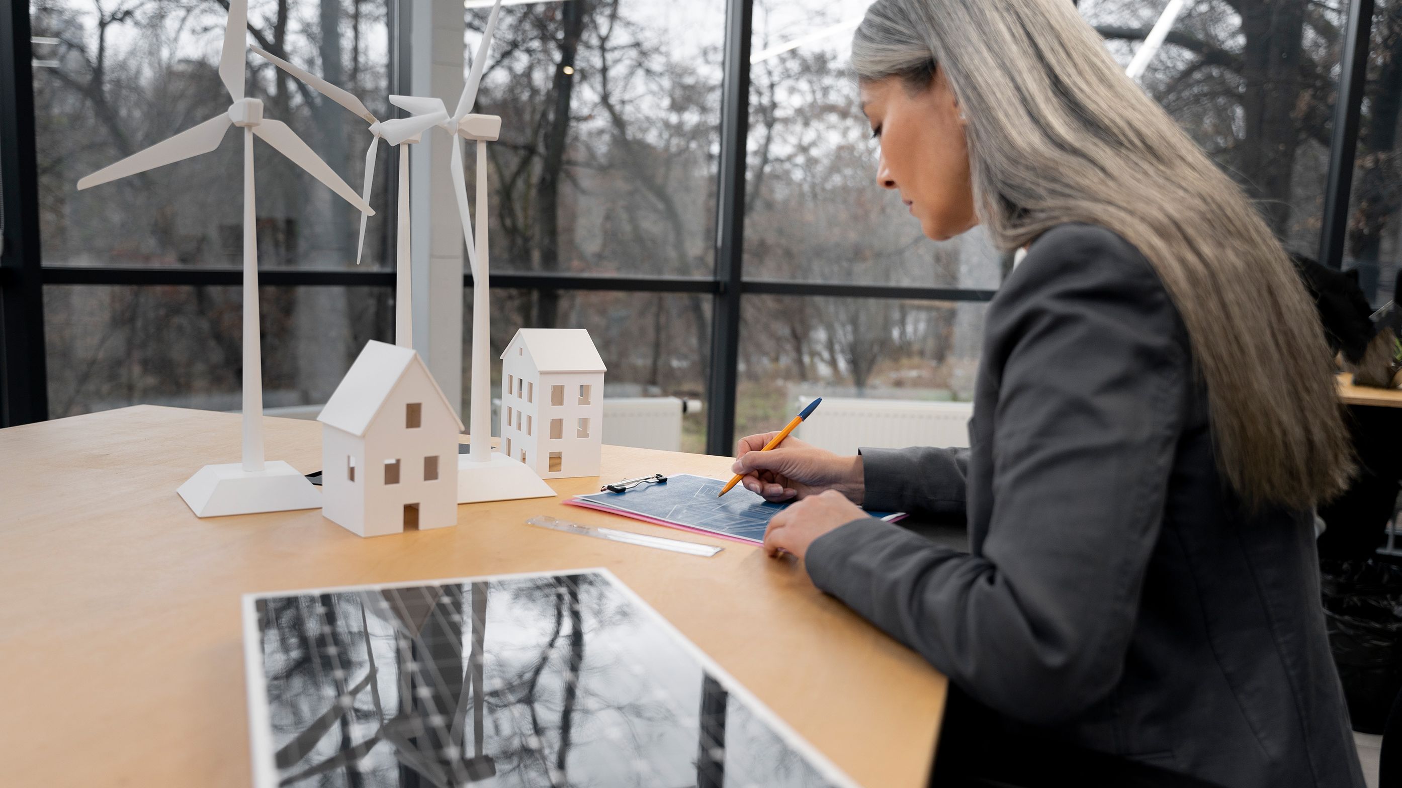 Ženska stoji ob mizi in si nekaj zapisuje, v svetlem in sodobnem interierju.