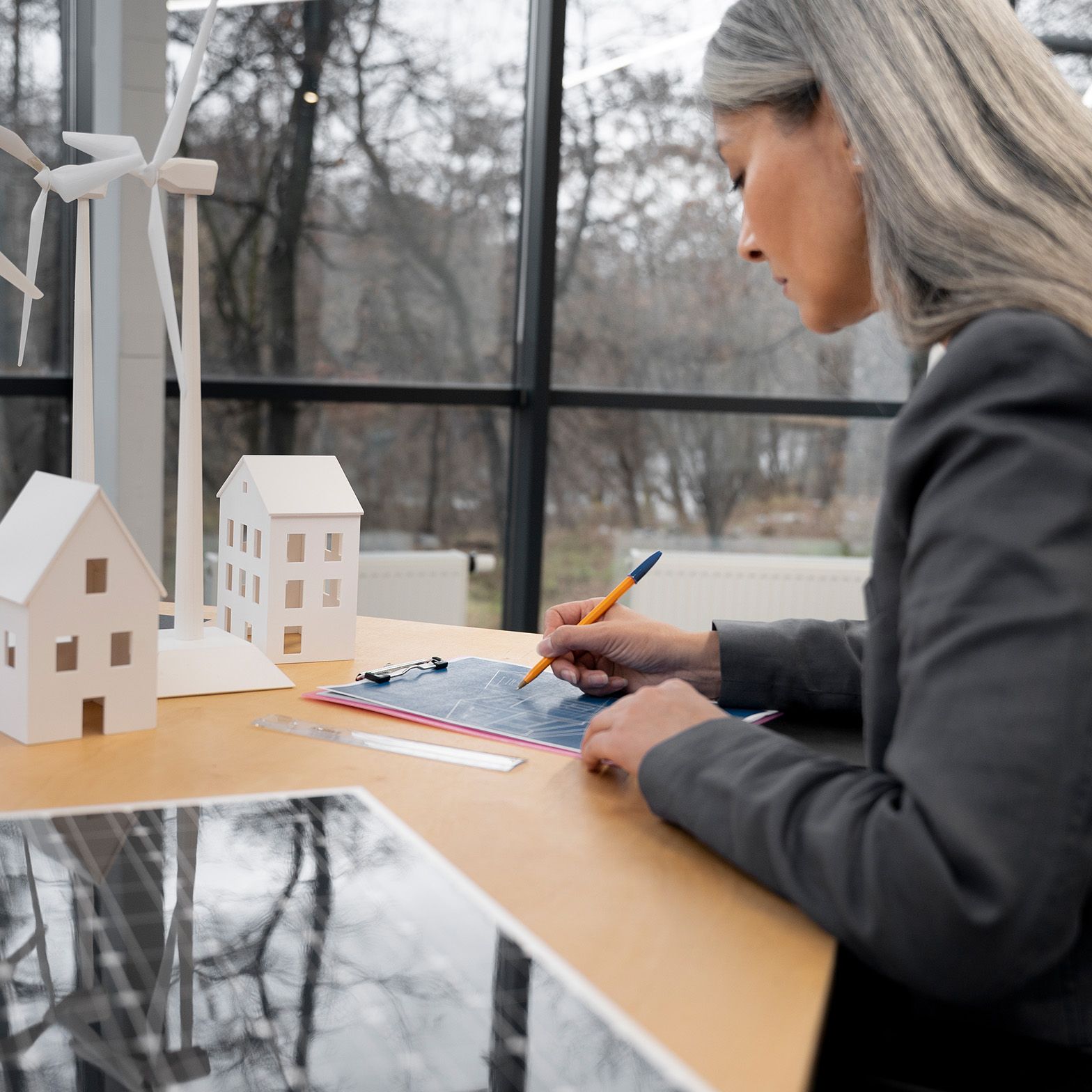 Ženska stoji ob mizi in si nekaj zapisuje, v svetlem in sodobnem interierju.