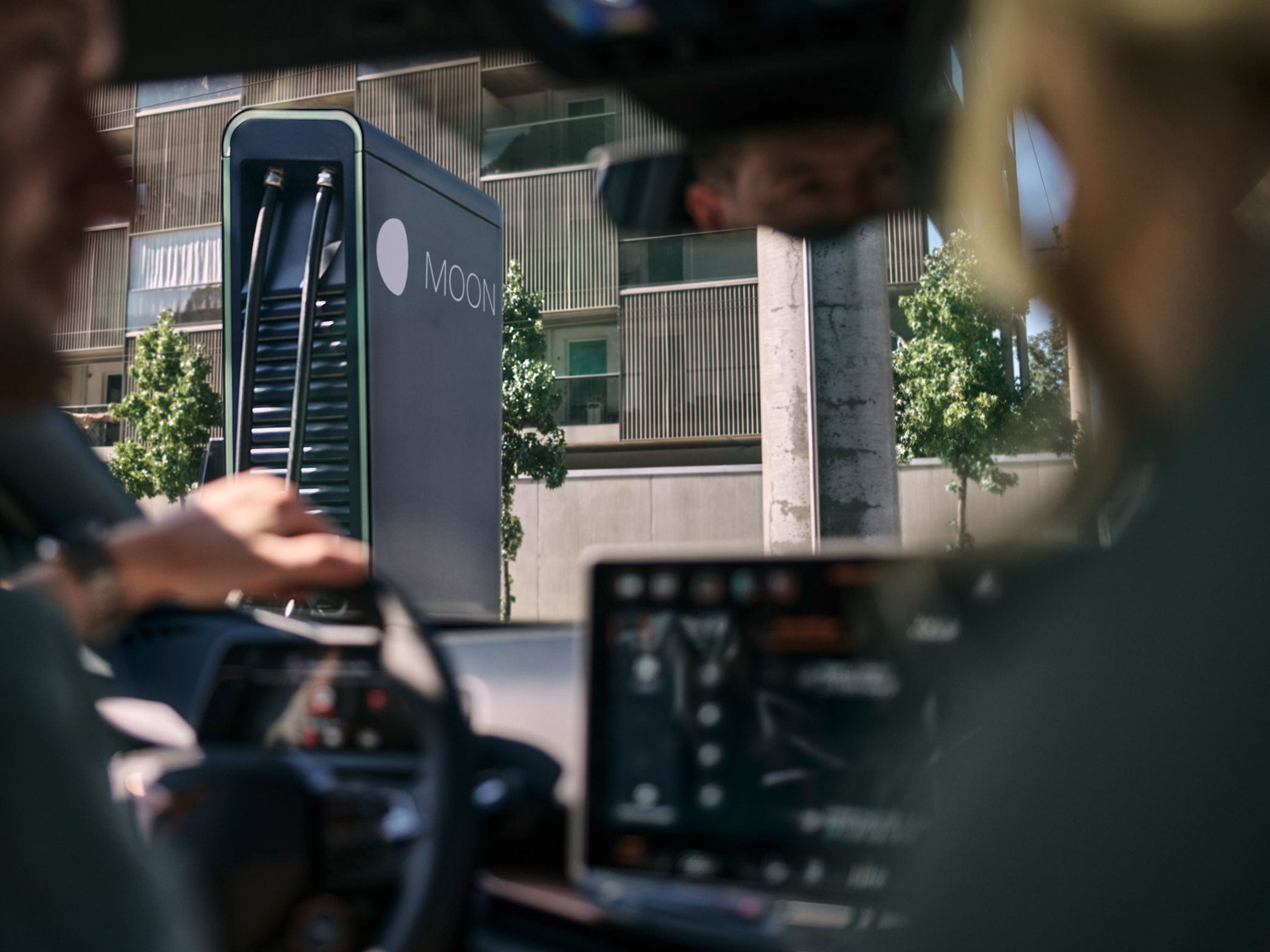 Dve osebi sedita v električnem vozilu pred hitro polnilno postajo.