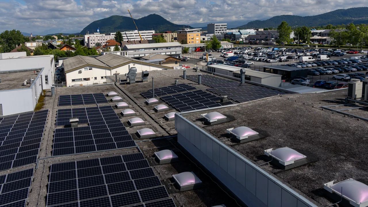 Stavba s sončno elektrarno na strehi, v ozadju pa hribovit teren.