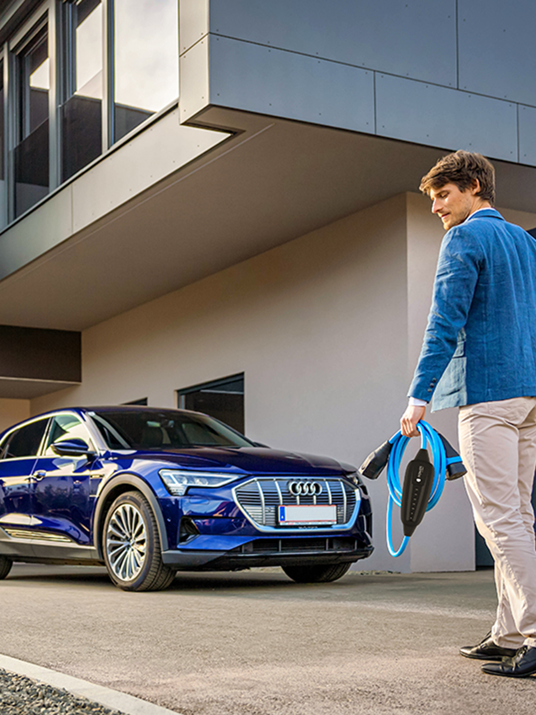 Oseba hodi proti električnemu avtomobilu s kablom v roki