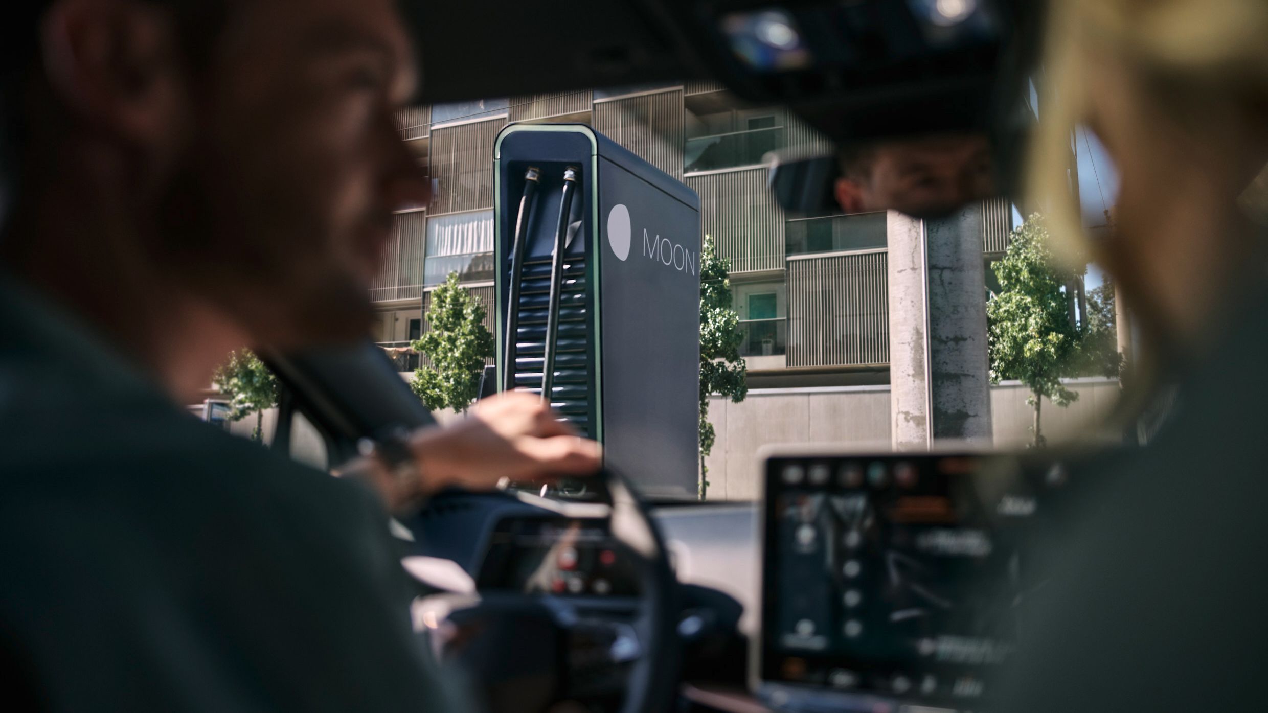 Dve osebi sedita v avtomobilu, parkiranem pred MOON hitro polnilno postajo.station