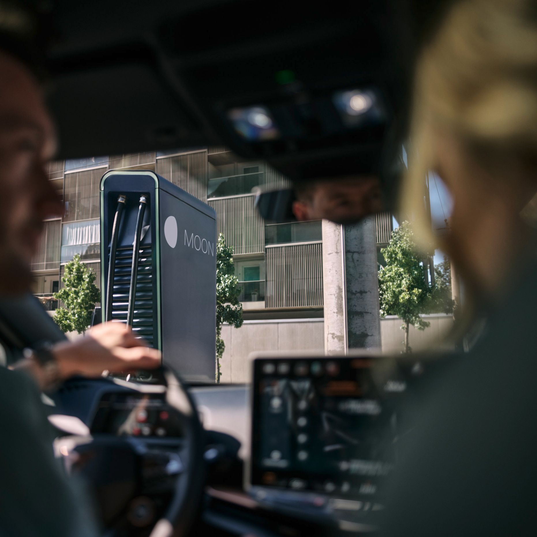 Dve osebi sedita v avtomobilu, parkiranem pred MOON hitro polnilno postajo.station