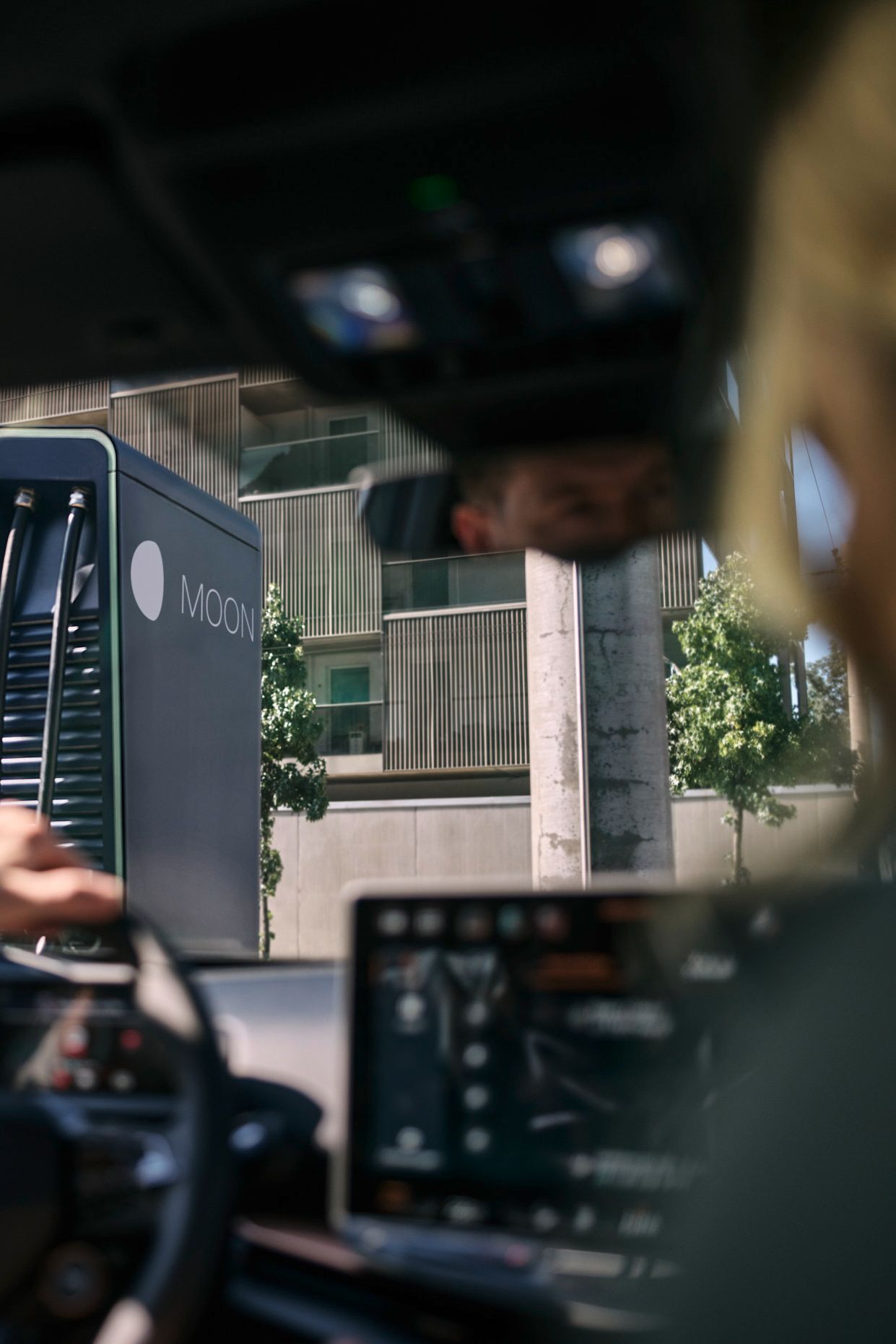 Dve osebi sedita v avtomobilu, parkiranem pred MOON hitro polnilno postajo.station