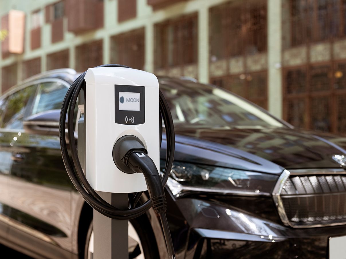 Stenska polnilnica pred električnim vozilom v turističnem okolju.