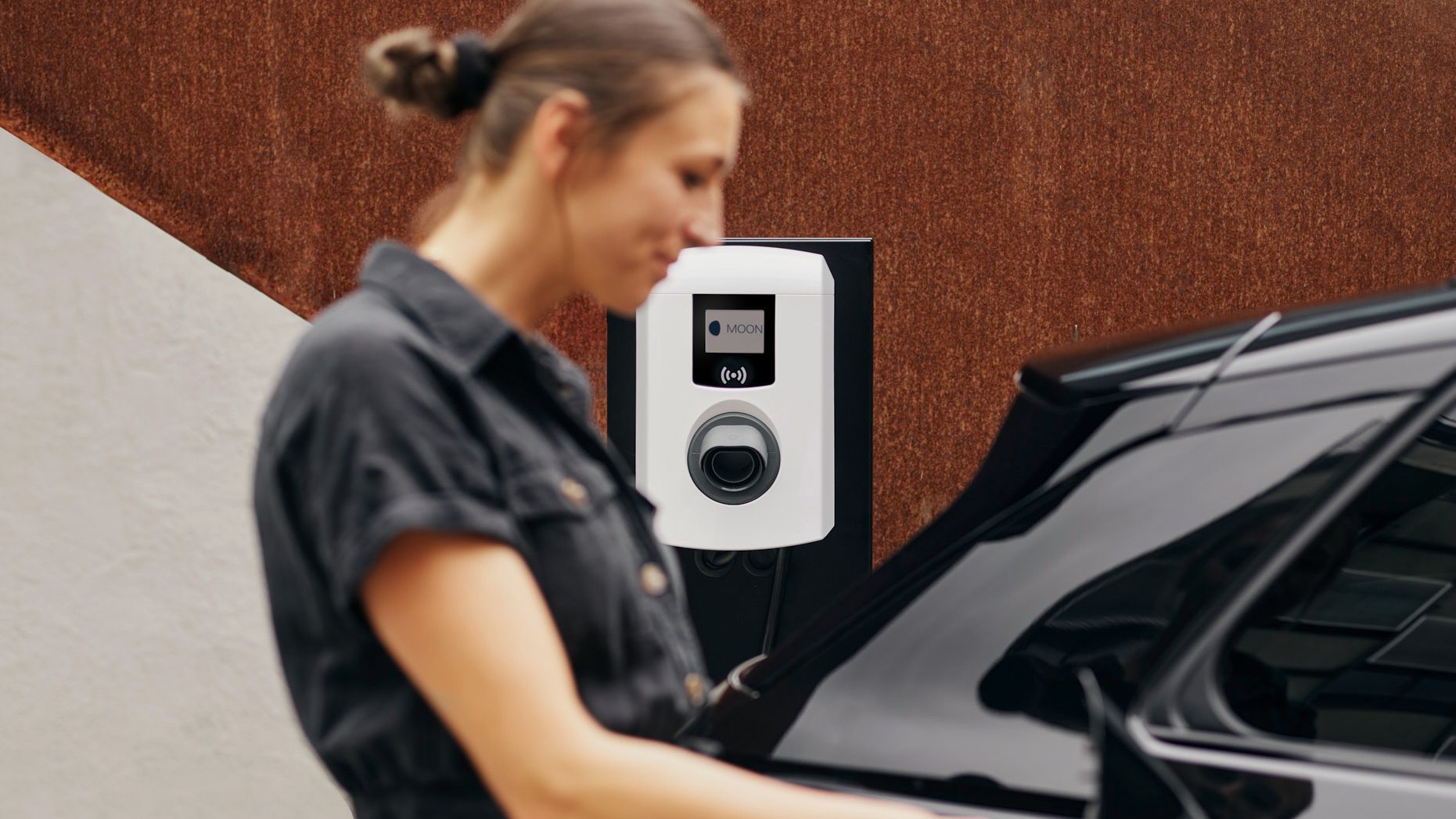 Ženska stoji ob mizi in si nekaj zapisuje, v svetlem in sodobnem interierju.