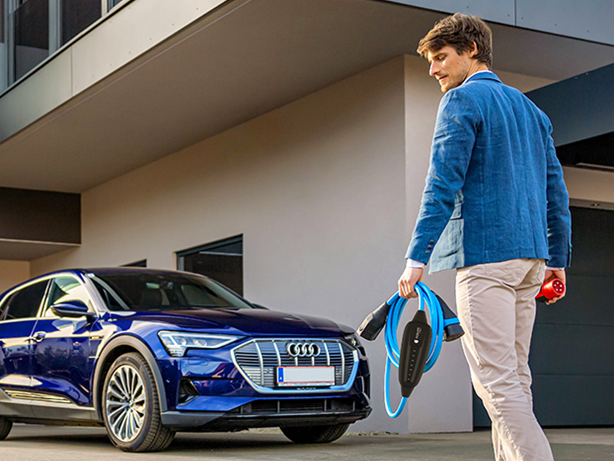 Oseba hodi proti električnemu avtomobilu s kablom v roki